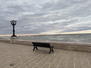 Empty bench facing the sea under a cloudy sky along a stone promenade